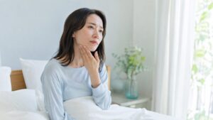 朝起きて顎の疲れが気になる女性(歯ぎしり・食いしばりのイメージ)