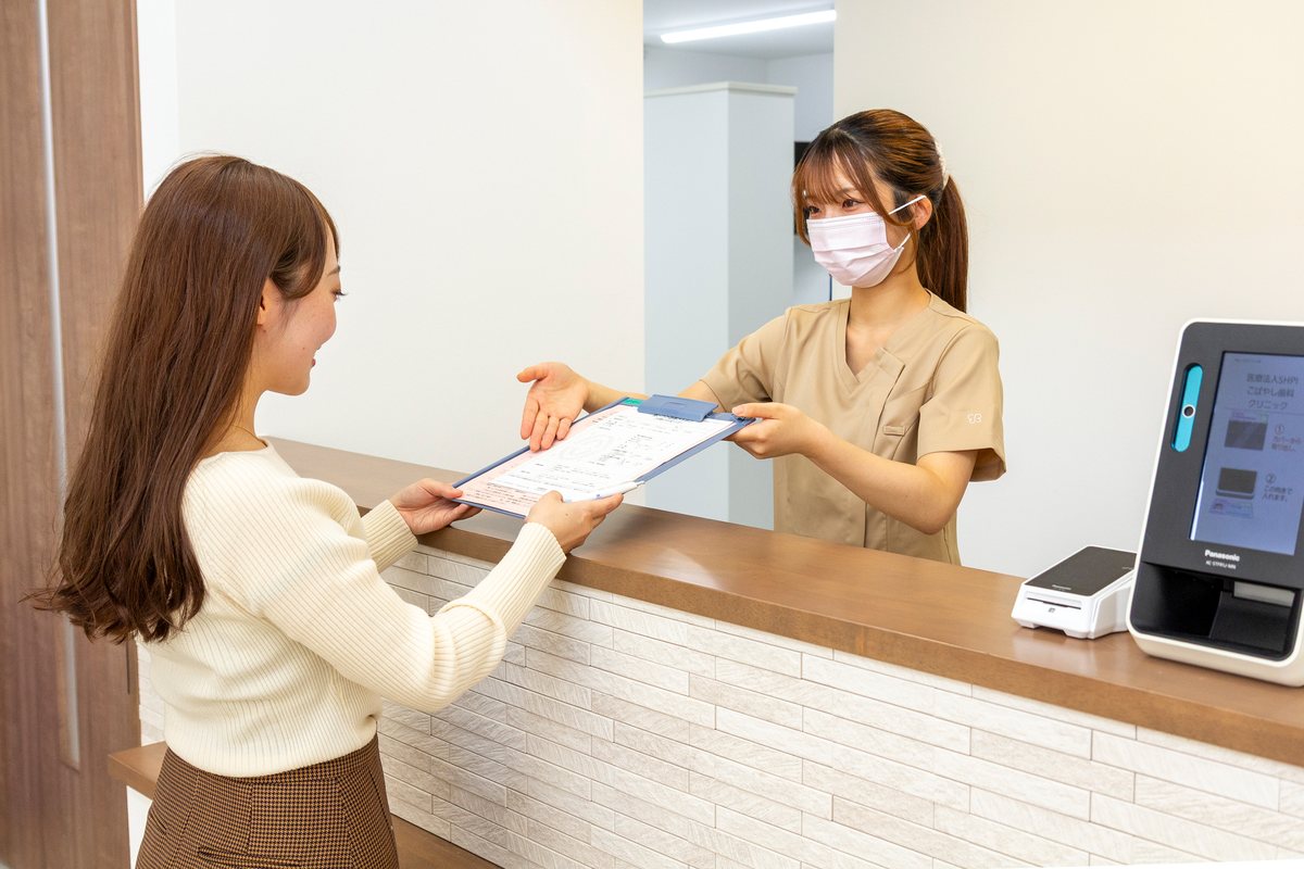 受付で書類をお渡ししながらご案内するスタッフと患者さま